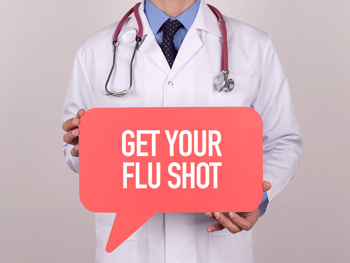 A doctor holding a sign that implores people to get their flu shot.
